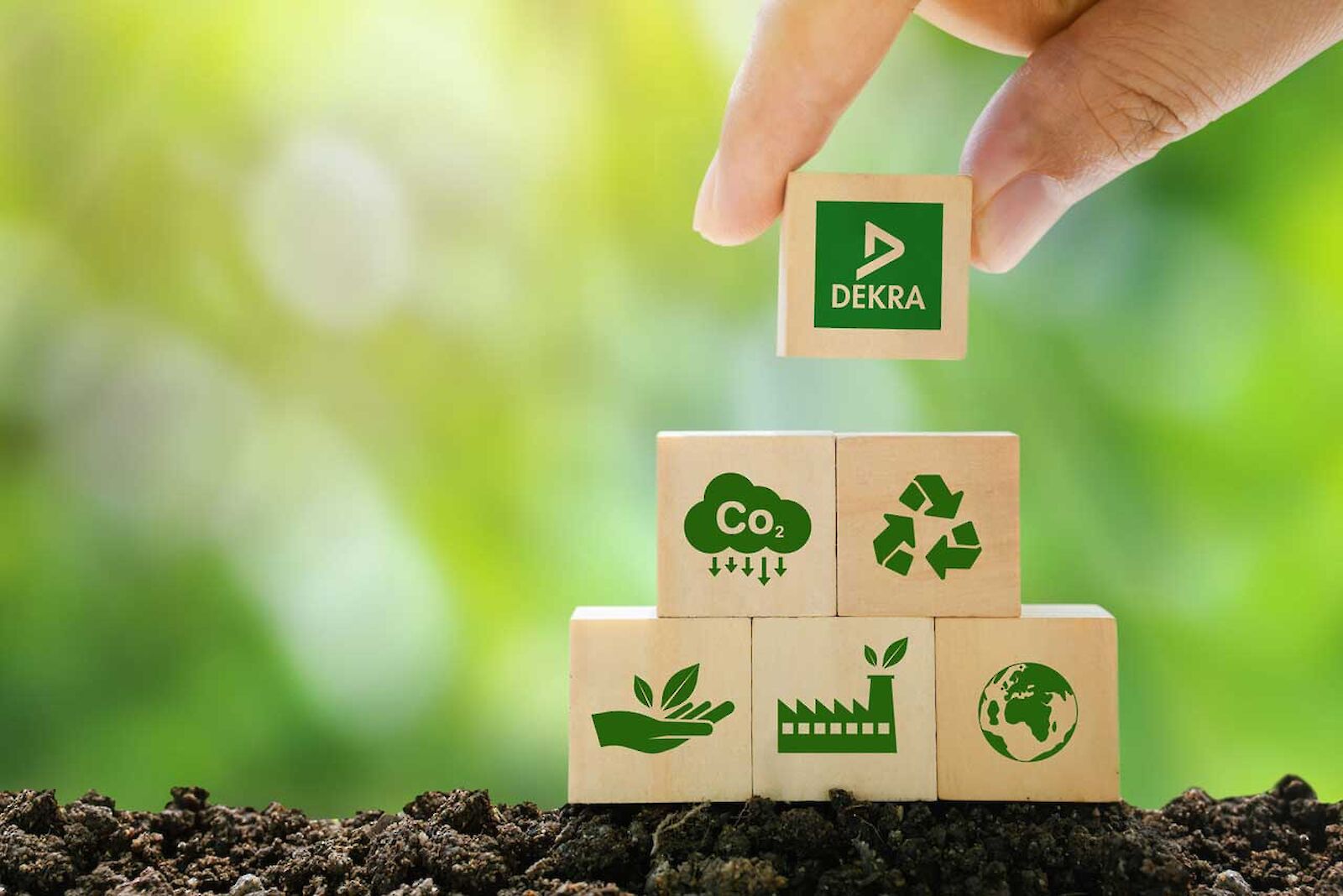 A hand stacks a pyramid of wooden blocks on which sustainability symbols and the DEKRA logo are depicted.